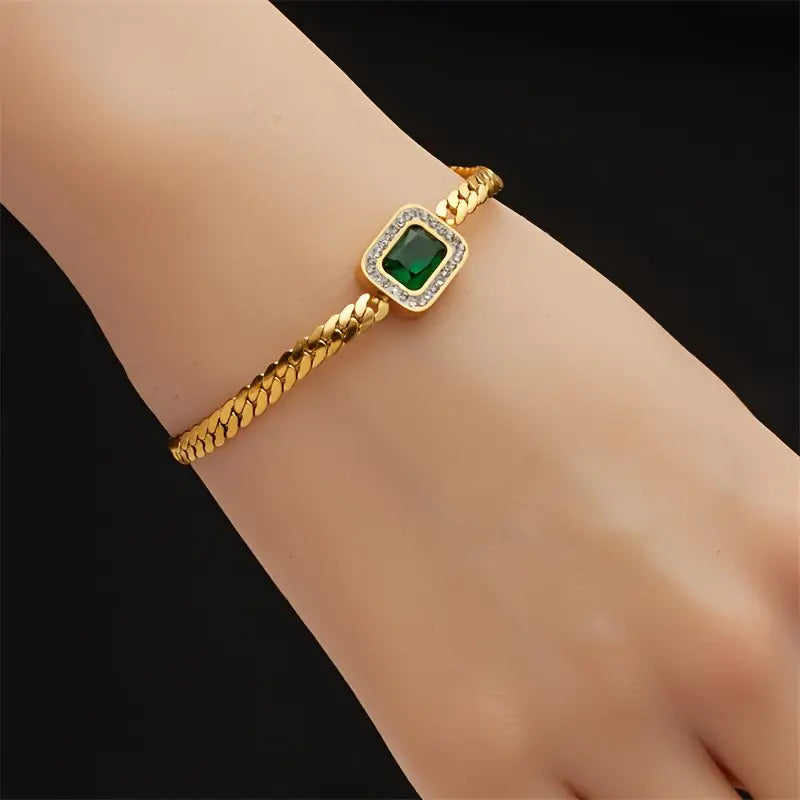 Feminint guld armbånd til kvinder, prydet med en strålende grøn krystal. Klassisk og luksuriøst design.