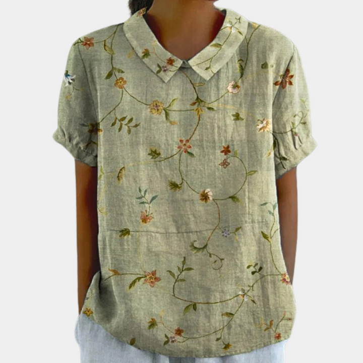 Farverig damebluse med smukt blomstermønster, korte ærmer og rund hals, perfekt til et stilfuldt hverdagslook.