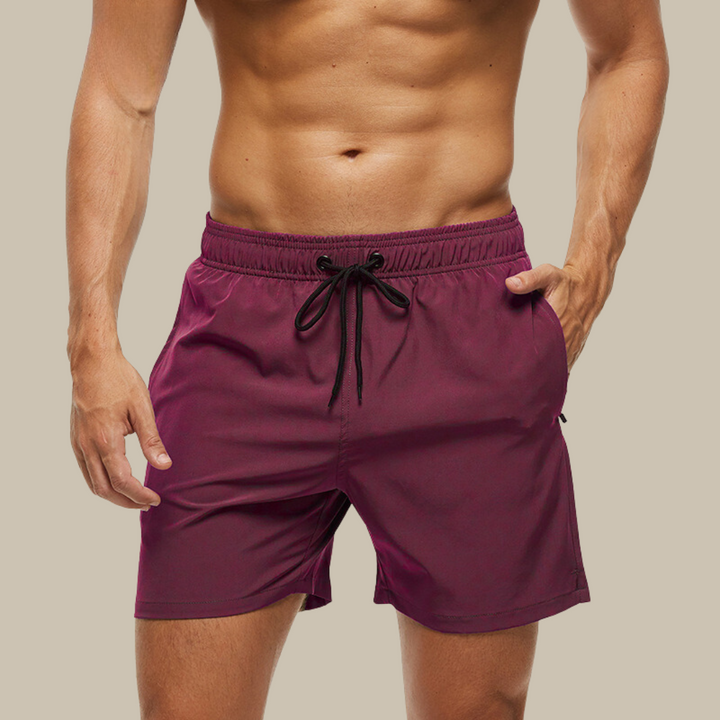 Hurtigtørrende herrebadeshorts med lynlåslommer og elastisk pasform, set forfra.